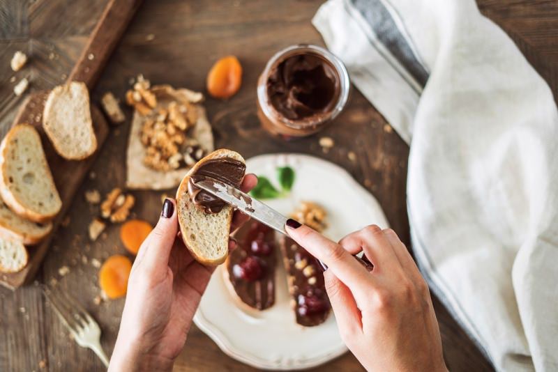 mani di donna spalma crema cioccolato nocciole fetta di pane tagliere albicocche