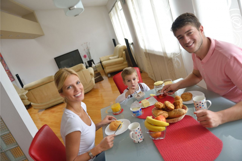 bella donna capelli biondi occhi azzurri mamma sorriso seduta a tavola con figlio bambino e uomo bello papà colazione cucina