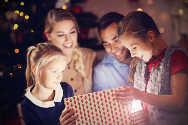 famiglia felice mamma pap figlia figlio sorridono mentre aprono regali di Natale davanti albero luci