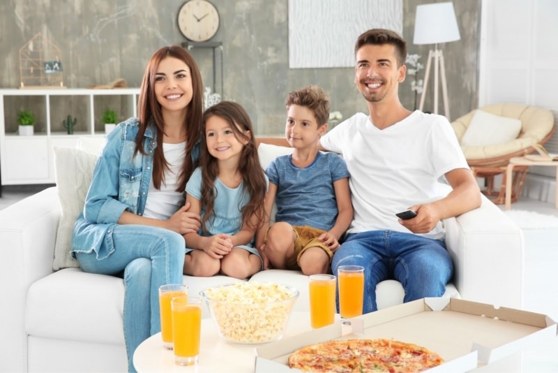 famiglia felice mamma pap figli sorrisi guardano tv mangiano pizza popcorn bicchieri succo arancia