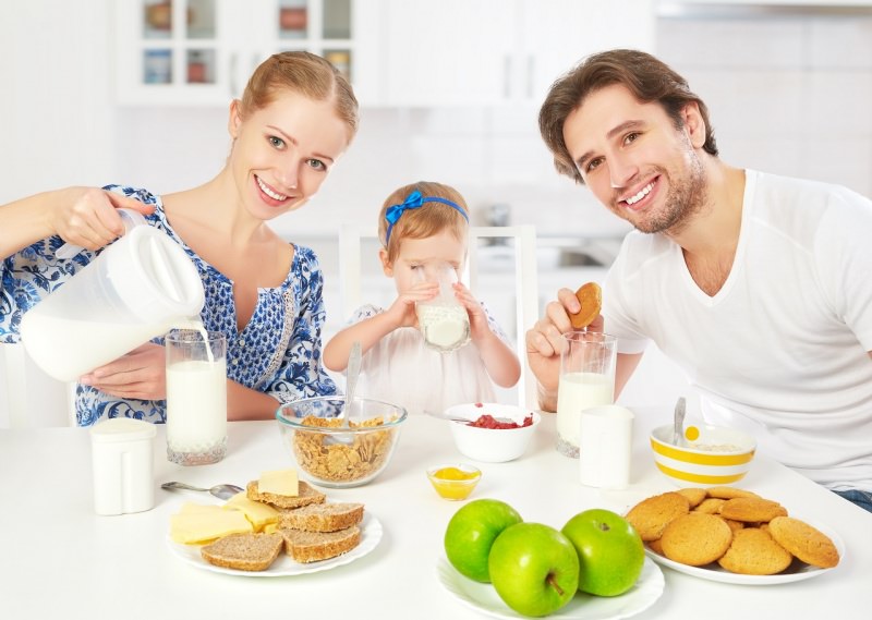 famiglia felice giovane donna capelli biondi sorrisi mamma bambina piccola figlia beve latte uomo pap biscotti latte