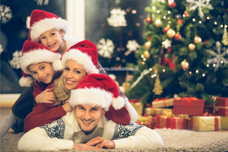 atmosfera natalizia in casa papà mamma bambini sdraiati davanti Alber di Natale magia luci oro rosso verde 