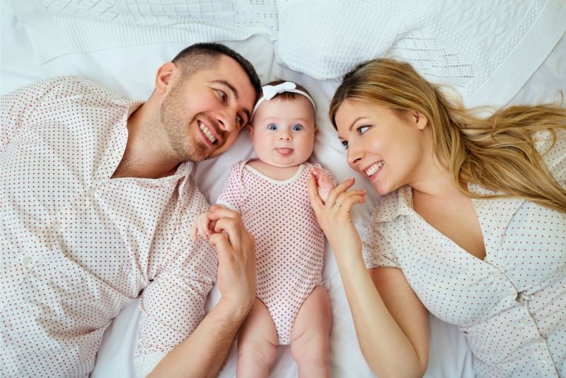 famiglia papà figlia neonata mamma nel lettone sorrisi coccole