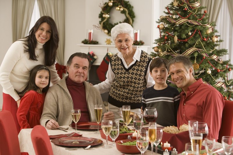 famiglia riunita tre generazioni attorno a tavola apparecchiata a festa albero di natale sorrisi