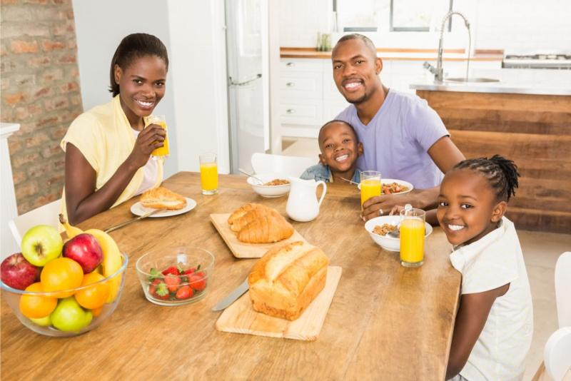 famiglia fa colazione al mattino donna mammauomo pap figlio figlia sorrisi ciotola fragole bicchieri spremuta arance cornetti croissanti vassoio