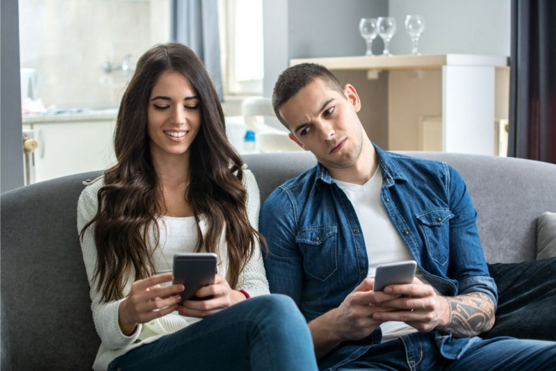giovane coppia seduta sul divano lui curioso guarda lo smartphone di lei