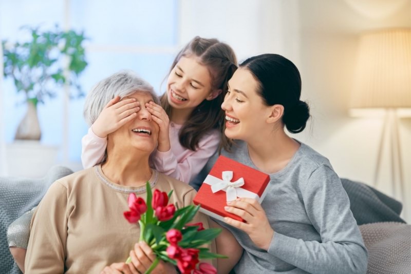 donna figlia adulta fa regalo mamma anziana bambina nipote pacco regalo fiori tulipani rossi