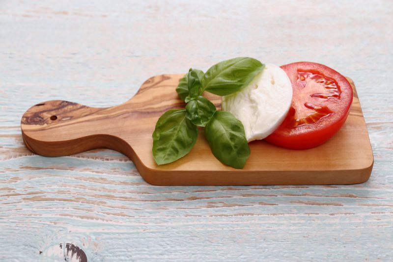 foglie di basilico mozzarella fiordilatte fetta di pomodoro rosso su tagliere di legno