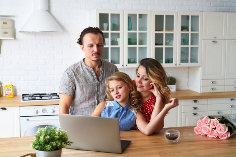 genitori pap mamma figlia adolescente navigare Internet laptop cucina