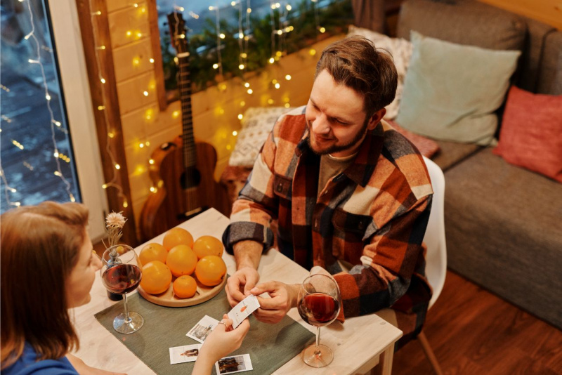 uomo e donna seduti tavolino giocano a carta sorridendo ghirlanda luci chitarra casa