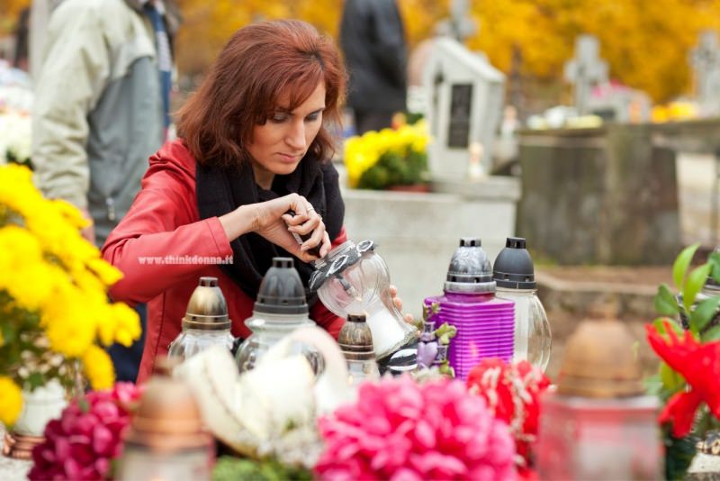 commemorazione defunti 2 novembre cimitero donna accende candela fiori crisantemi 