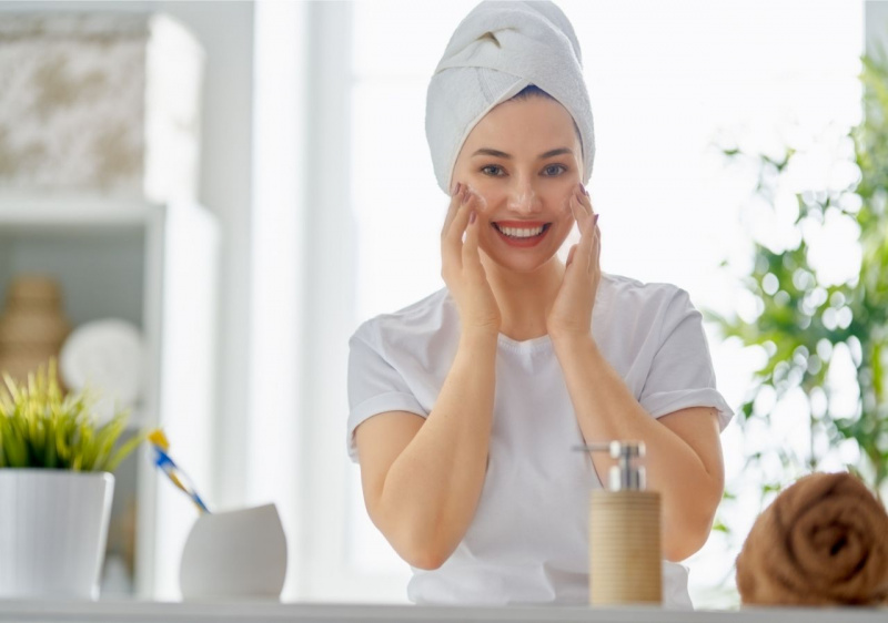 viso donna sorridente che applica crema sul viso guardandosi allo specchio