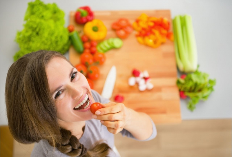 giovane bella e sorridente donna mangia pomodoro frutta e verdure sul tavolo