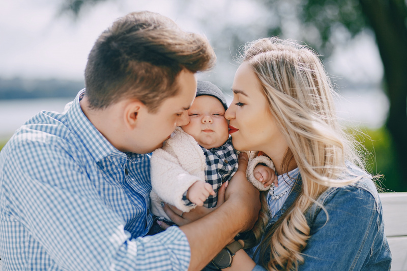 mamma e pap proteggono figlio neonato coccole baci uomo camicia quadri bianco azzurro mamma capelli biondi camicia jeans