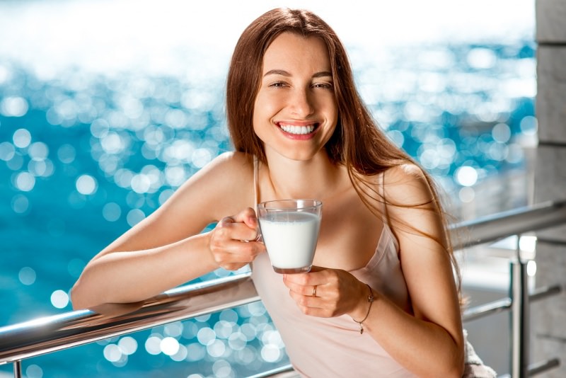bella donna beve bicchiere latte sul balcone vista mare