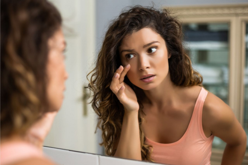 occhiaie segni di stanchezza bella donna capelli lunghi ricci castani si specchia top canotta rosa