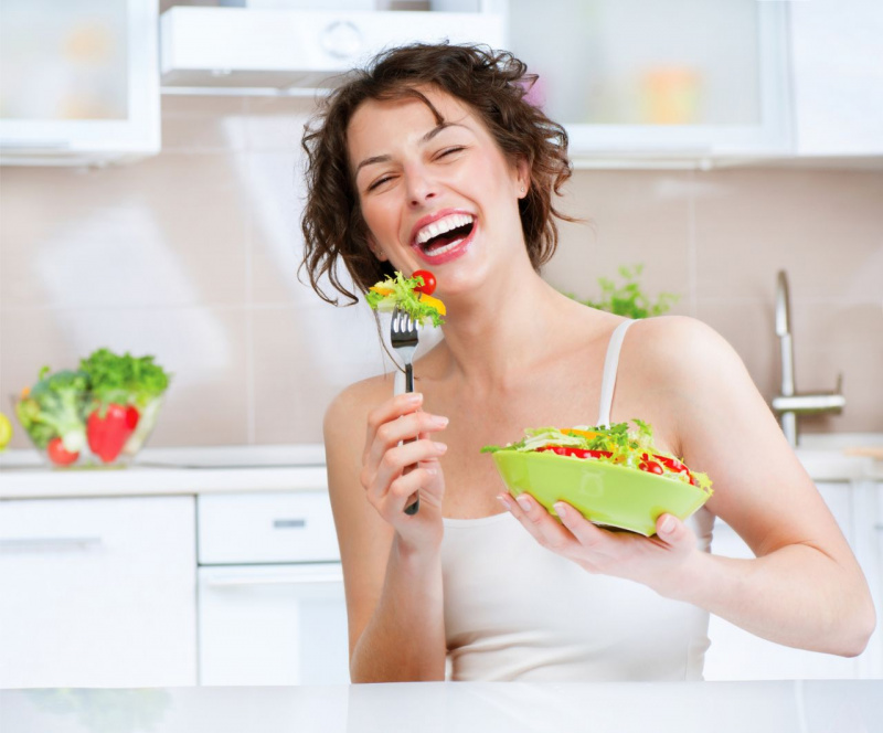 bella donna sorridente mangia verdure in cucina