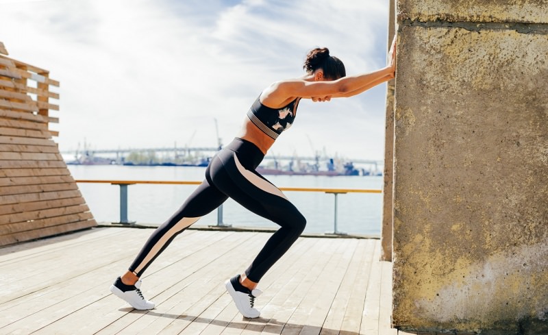 donna atletica mani al muro stretching terrazzo cielo