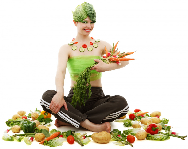 viso donna con foglie cavolo in testa fette cetriolo pomodori sulla scollatura tiene in braccio mazzo carote ravanelli asparagi patate peperoni 