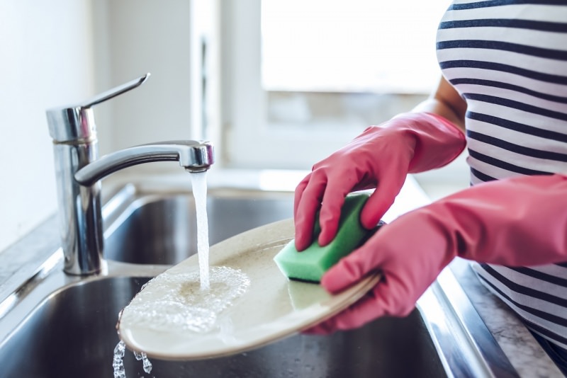 giovane donna lava piatti guanti di gomma