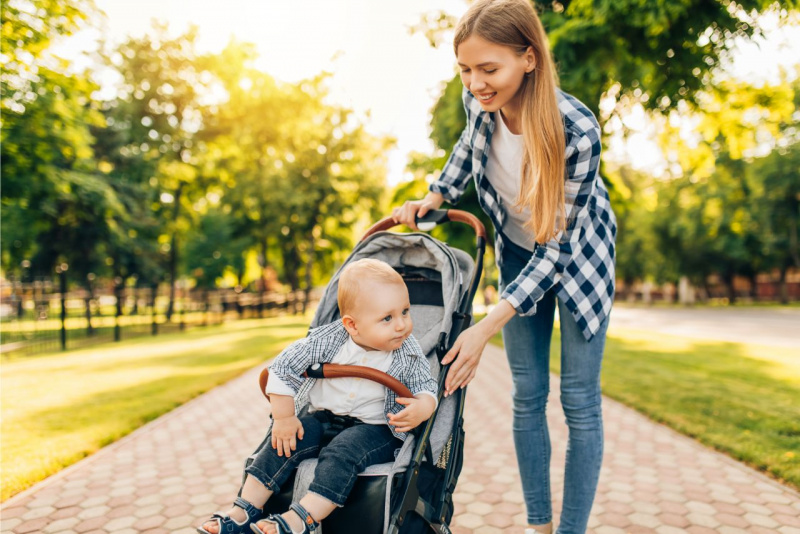 viale alberi bambino piccolo beb jeans sandali camicia maglietta bianca seduto passeggino con mamma sorridente capelli lunghi camicia quadri bianco nero