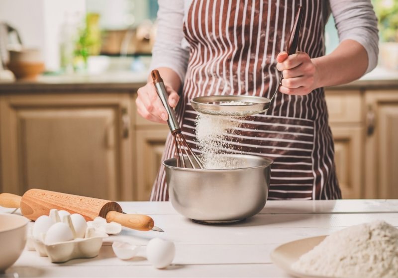 giovane donna grembiule setaccia farina impasto plumcake uova