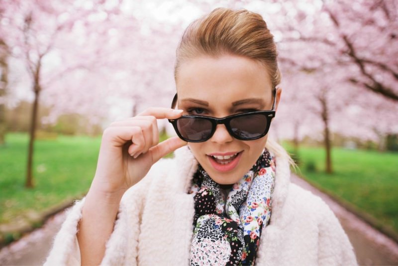 giovane donna sveglia fa l'occhialino occhiali da sole alberi fiori rosa ciliegio