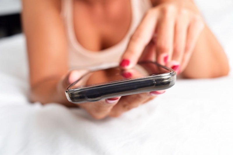 donna usa smartphone a letto manda messaggio sexting
