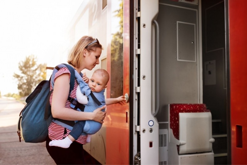 giovane donna sale in treno con zaino fasciatoio sulle spalle e bambino neonato marsupio