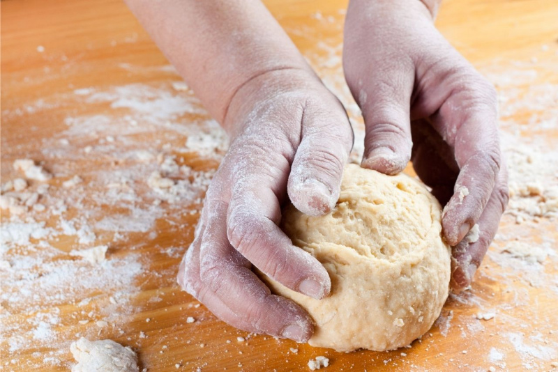 mani impastano pasta per cassatelle su piano lavoro con farina