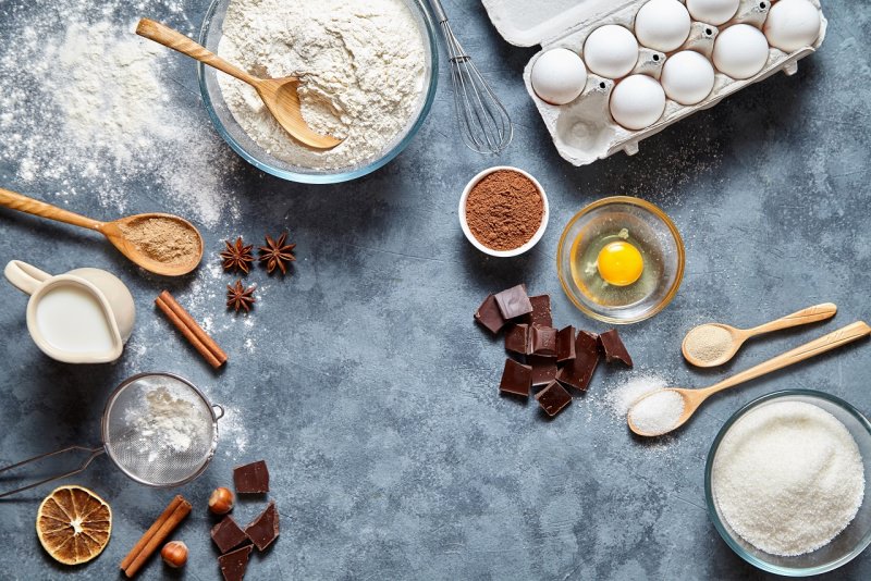 ingredienti per brownies ciotola farina mestolo legno zucchero uova latte cioccolato nocciole