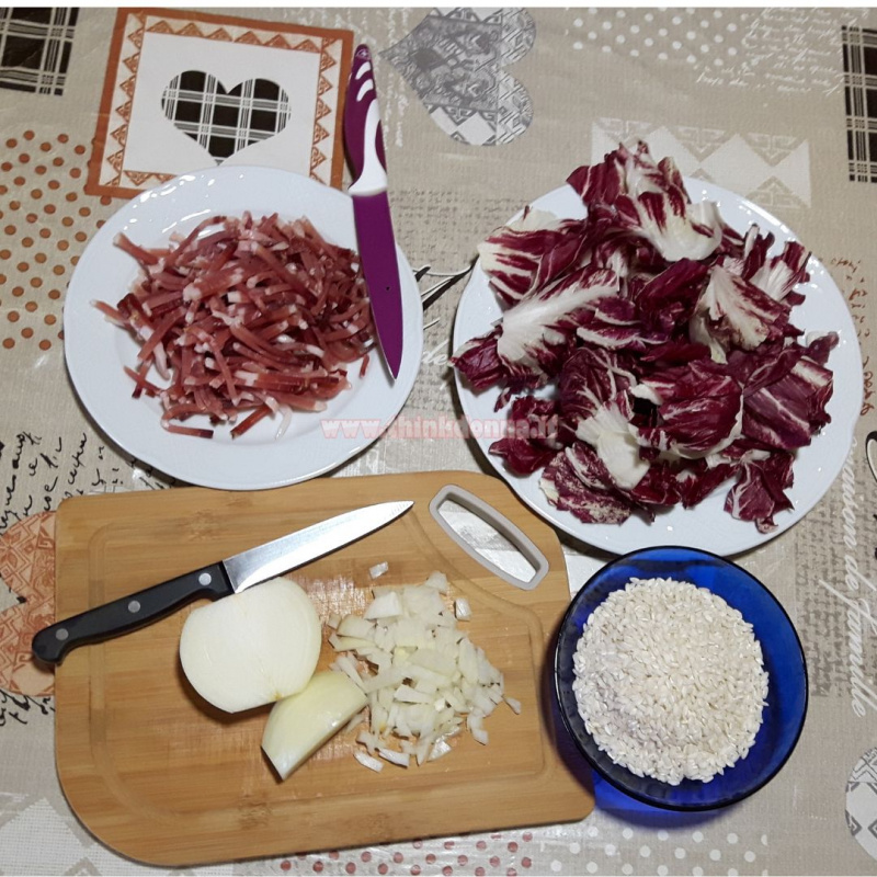 tavola con piatto speck tagliato a strisce radicchio rosso tagliere di bamb coltello cipolla ciotola vetro blu con riso