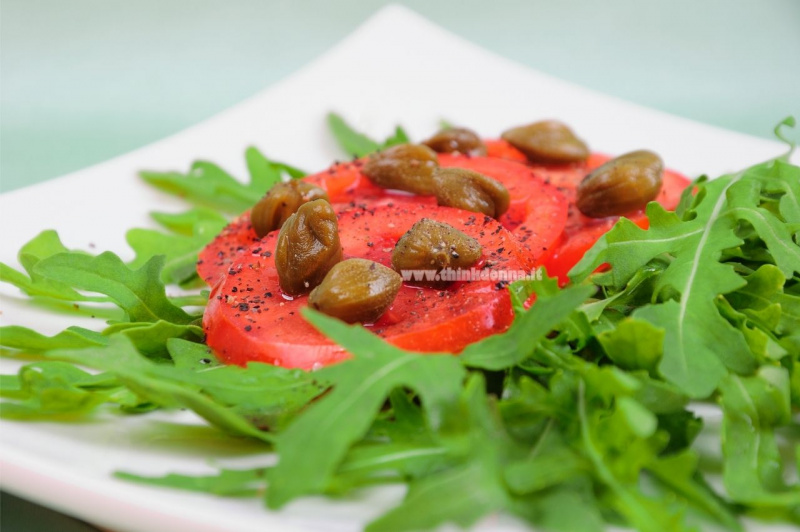 contorno rucola foglie fette pomodori rossi capperi su piatto