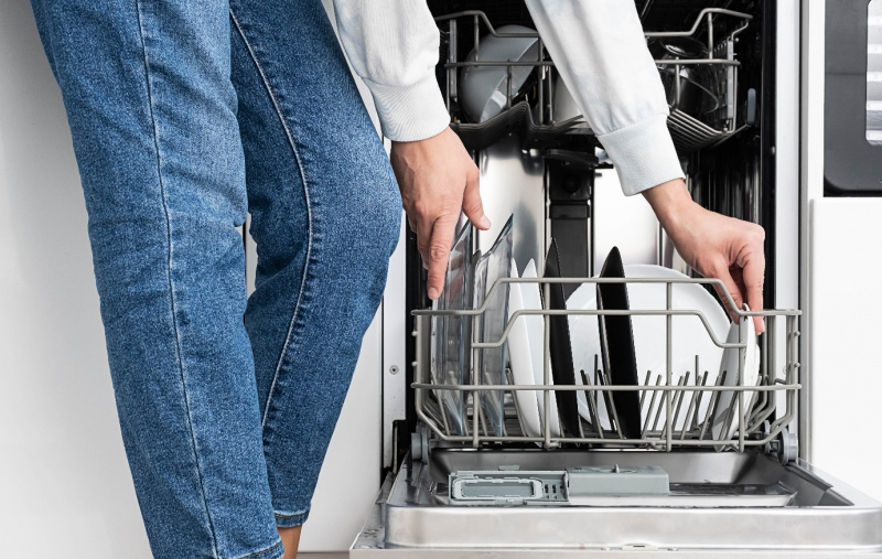 donna con jeans carica lavastoviglie piatti