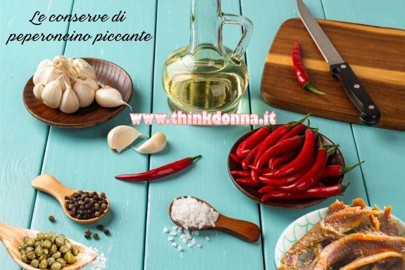 preparazione conserva peperoncini rossi piccanti sott'olio con capperi sotto sale spicchi aglio pepe grani alici su piano legno azzurro