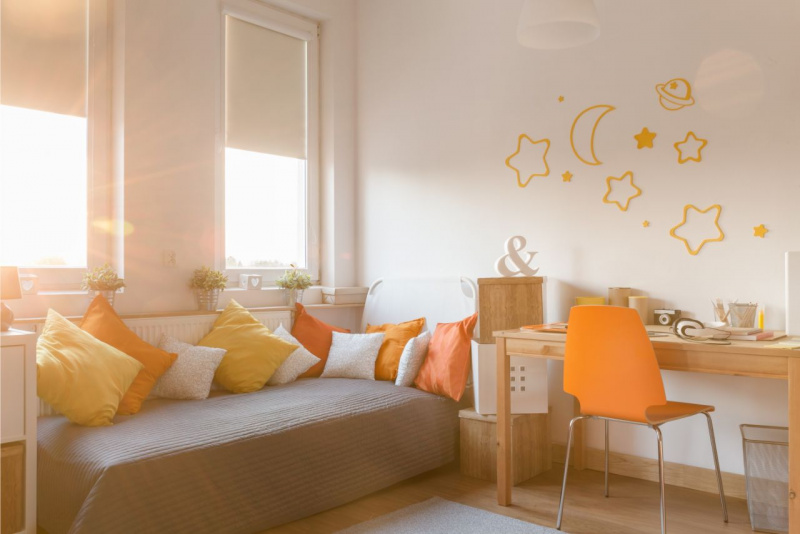 letto pieno di cuscini colori vivaci giallo arancione finestra luminosa scrivania angolo studio