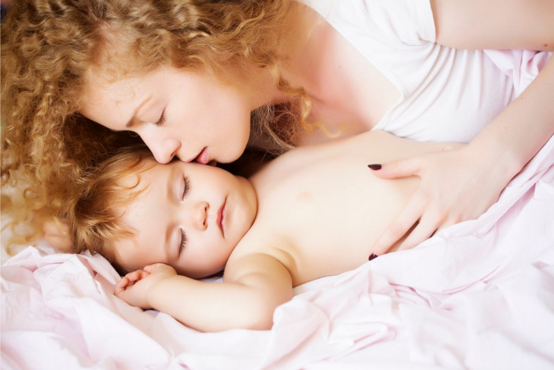 bella donna capelli ricci biondi bacia sulla guancia bambino neonato bellissimo mentre dorme