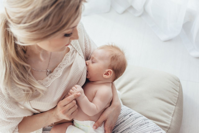 donna capelli biondi tiene in braccio figlio neonato mentre lo allatta al seno allattamento