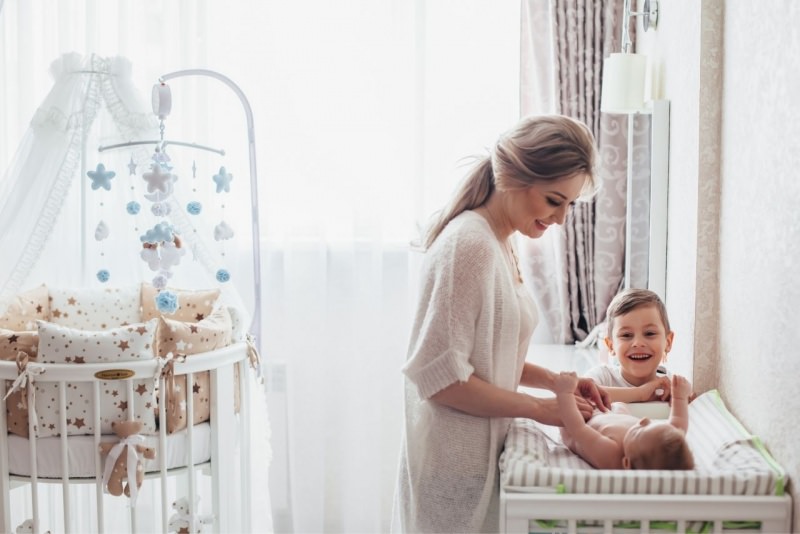 mamma sorridente cambia pannolino neonato nella nursery con figlio primogenito culla 