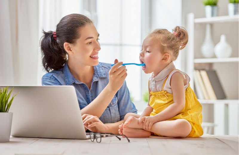 donna mamma lavora laptop da casa mentra da da mangiare alla figlia piccola