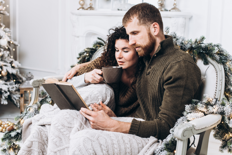 coppia innamorati sul divano leggono libro lei beve t abbraccio albero di natale