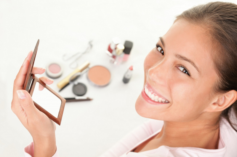 viso bella donna sorridente si prepara al makeup specchietto prodotti per il trucco