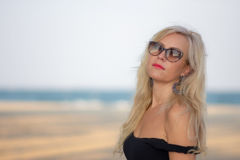 donna cinquanta anni capelli biondi occhiali da sole top nero mare