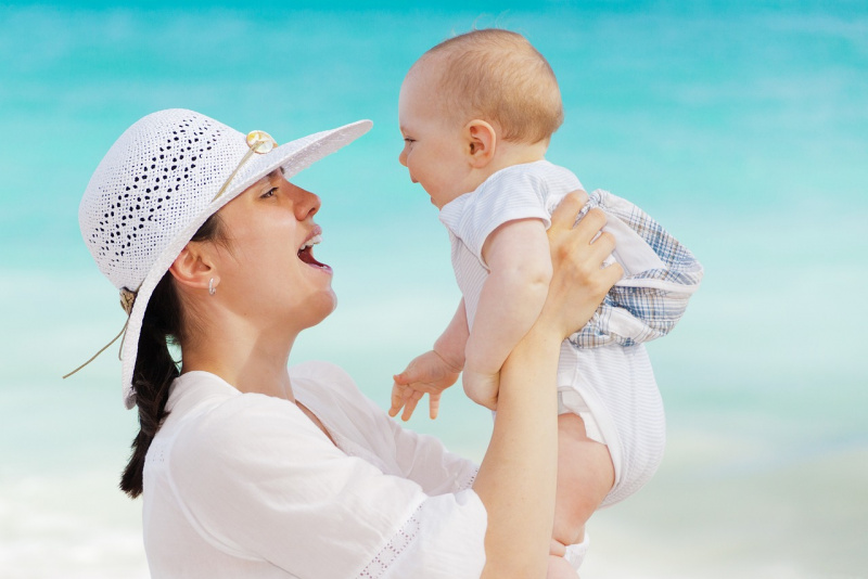 mamma solleva in aria bambino neonato sorriso cappello bianco pannolino