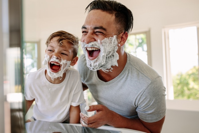 papà e figlio si divertono in bagno con schiuma da barba allo specchio