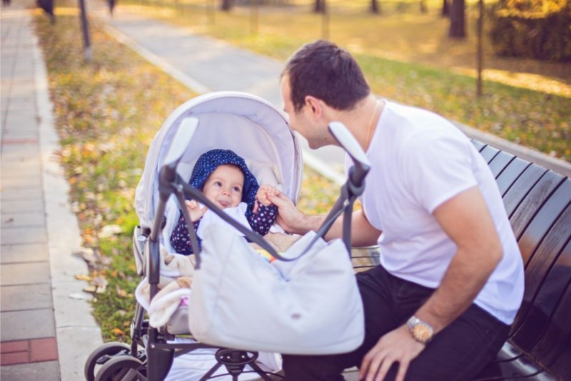 papà con passeggino figlio bambino al parco borsa