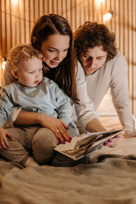 giovane famiglia con bambino piccolo leggono libro sul letto luci
