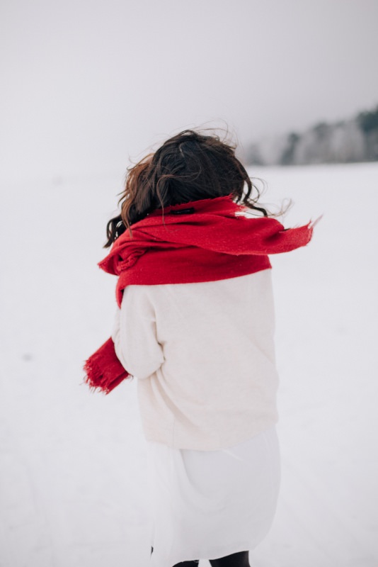 donna di spalle maglione bianco sciarpa rossa neve inverno