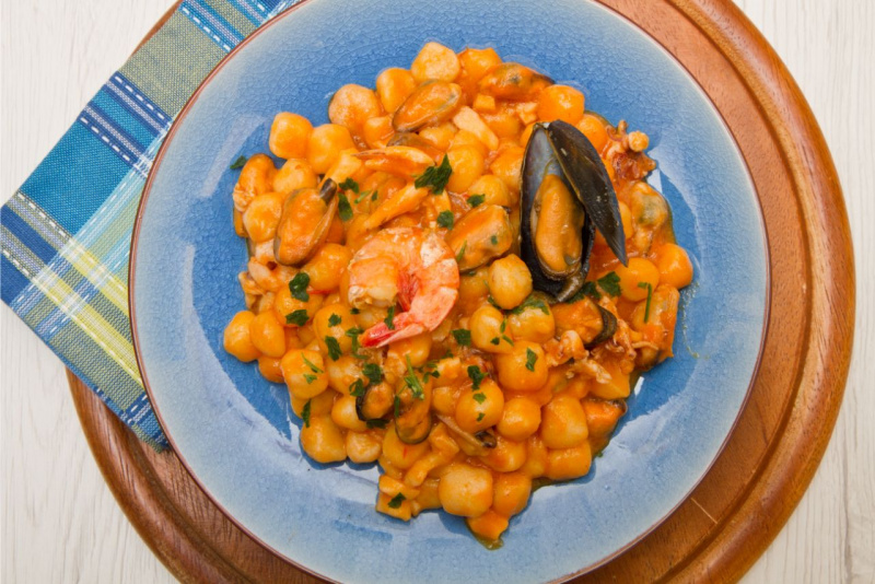 primo piano dall'alto gnocchi ai frutti di mare con sugo pomodoro cremosi cozze gamberi vongole piatto ceramica azzurro sottopiatto legno