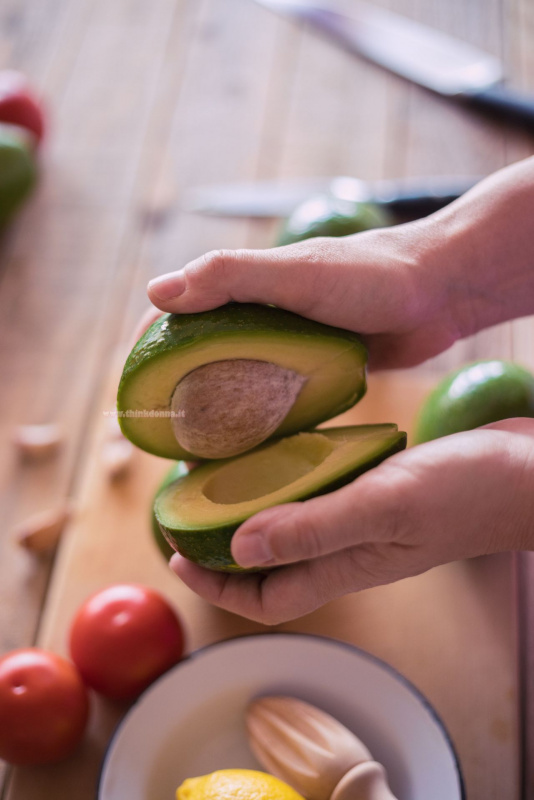 avocado aperto in due parti con le mani pomodori spremiagrumi di legno